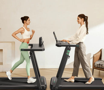 Two women use treadmills: one exercises in sportswear, while the other works on a laptop in casual attire.